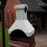 Grillkamin im Garten, dahinter das Saunahäuschen